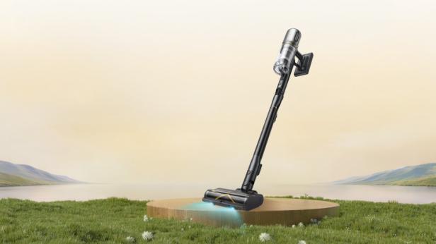 Ein moderner kabelloser Staubsauger steht auf einer runden Plattform in einer grünen Landschaft.