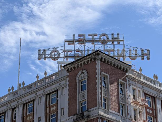 Hotelgebäude mit großem Schild auf dem Dach vor blauem Himmel mit Wolken.