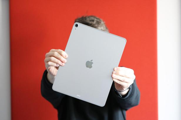 Person hält ein silbernes iPad Air 13 vor rotem Hintergrund in beiden Händen.