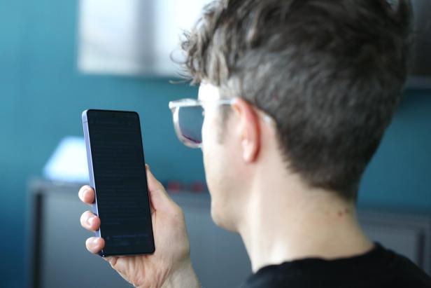 Eine Person hält ein Smartphone mit kaum lesbarem, abgedunkeltem Display in der Hand.