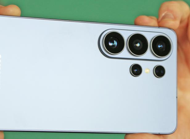Rückseite eines Smartphones mit vier Kameralinsen und LED-Blitz vor grünem Hintergrund.