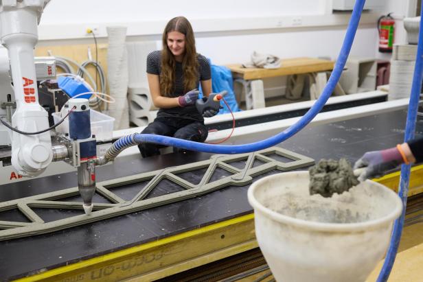 Eine Forscherin der Hochschule Campus Wien überwacht den 3D-Betondruck eines Fachwerkträgers mit einem Roboterarm im High Tech Campus.