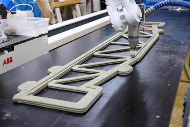 Ein 3D-Drucker trägt Beton schichtweise zu einem Fachwerkträger auf einer Platte auf.