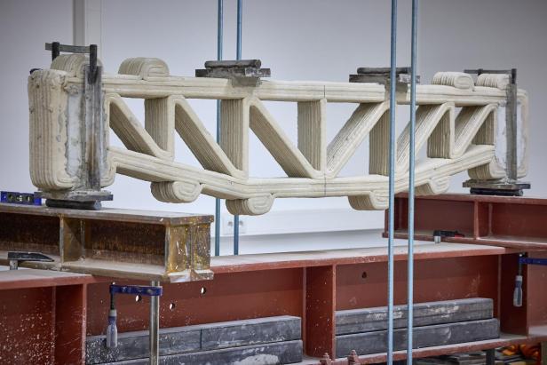 3D-gedruckter Betondeckenträger mit Fachwerkstruktur in einer Prüfapparatur eingespannt.