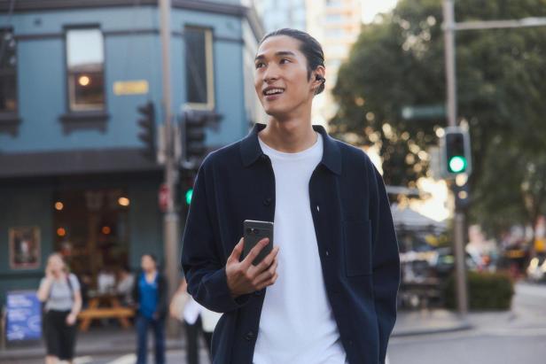 Eine Person trägt die Sony LinkBuds Clip im Ohr und geht entspannt mit Smartphone in der Hand durch die Stadt.