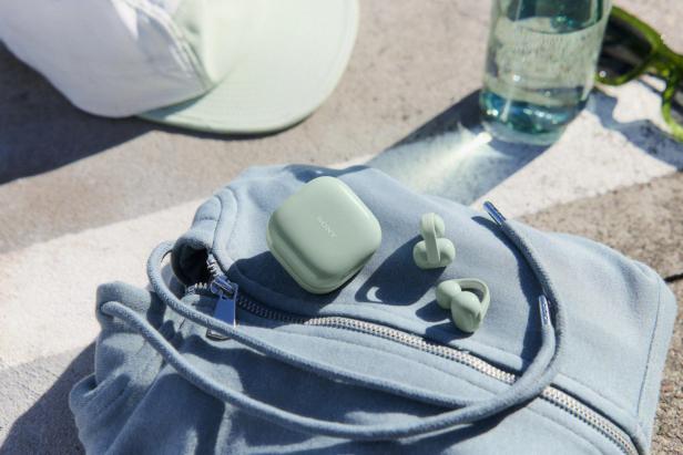 Sony LinkBuds Clip in Pastellgrün mit Ladecase auf einem hellblauen Rucksack im Sonnenlicht.
