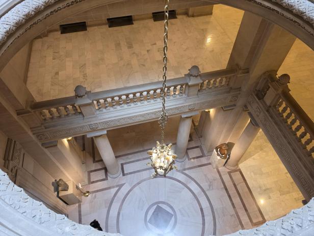 Blick von oben auf eine prunkvolle Marmortreppe mit Kronleuchter und Statuen im Rathaus.