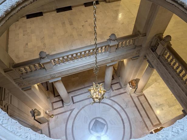 Blick von oben auf eine prunkvolle Marmortreppe mit Kronleuchter und Statuen im Rathaus.