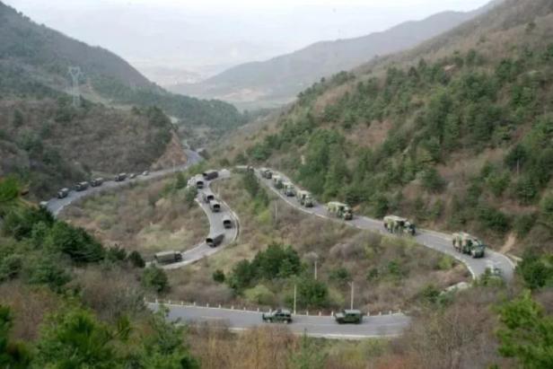 Eine kurvige Gebirgsstraße auf der mehrere Militärfahrzeuge im Convoy fahren