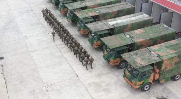 militärische Lkw stehen bereit während die Fahrer davor in Zweierreihe gehen