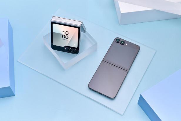 Zwei zusammengeklappte und aufgeklappte faltbare Smartphones auf hellblauem Untergrund.
