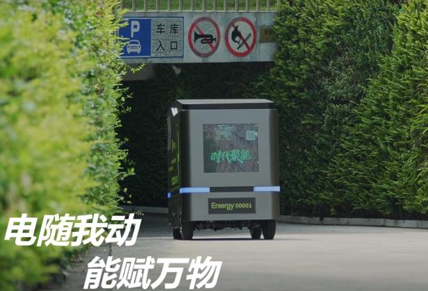 Lade-Roboter von Eraergy fährt auf einer Straße zwischen grünen Hecken zu einer Parkplatzeinfahrt.