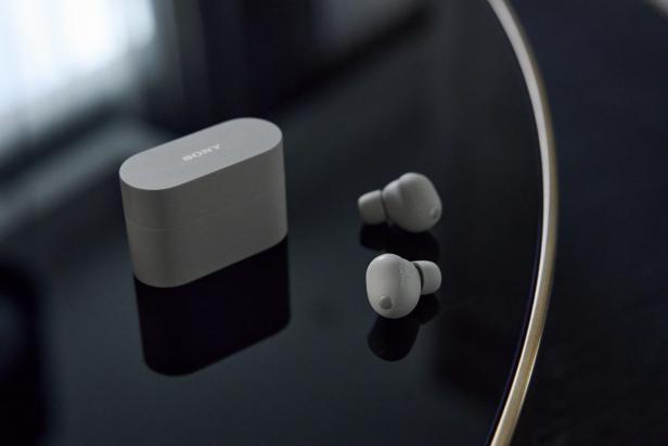 Graue Sony WF-1000XM6 In-Ear-Kopfhörer mit passendem Ladecase auf schwarzer Oberfläche.