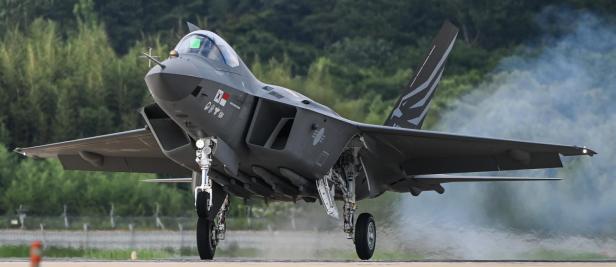 Kampfjet KF-21 bei der Landung auf einer Startbahn vor bewaldeter Bergkulisse.