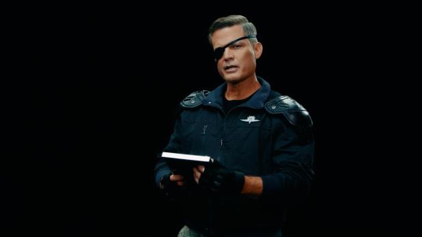 Ein Mann mit Augenklappe und Uniform steht vor schwarzem Hintergrund