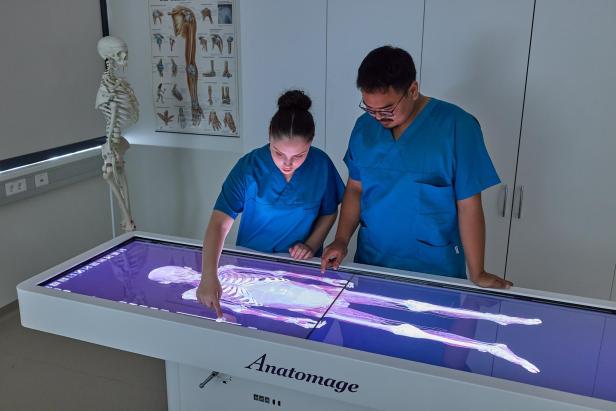 Zwei Personen in blauer Pflegekleidung arbeiten an einem digitalen Anatomietisch.