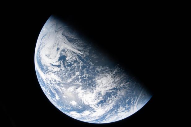 Die Erde halb im Sonnenlicht, halb im Schatten, vor schwarzem Weltraum.