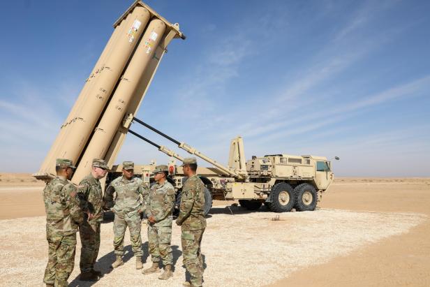 Mehrere Soldaten stehen vor einem mobilen Raketenabwehrsystem des Typs THAAD, das auf einem Militärfahrzeug in einer Wüstenumgebung aufgerichtet ist.