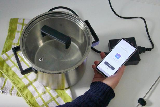 eine Hand hält ein Smartphone mit der Wired Cooker App neben den Topf