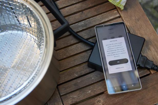 Smartphone das Hinweise zur Frittierfunktion anzeigt, neben dem Wired Cooker mit Korb-Einsatz