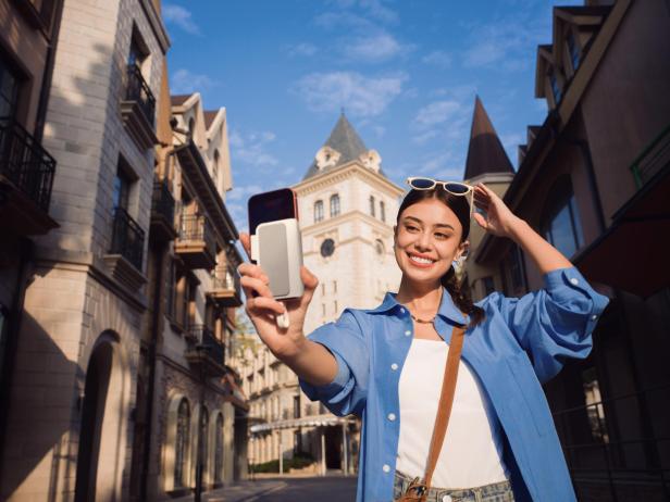 Frau macht Selfie mit Smartphone und magnetischem Zweitbildschirm auf einer sonnigen Straße.
