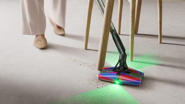 Dyson PencilVac saugt Schmutz unter einem Stuhl, grünes Licht beleuchtet den Boden.