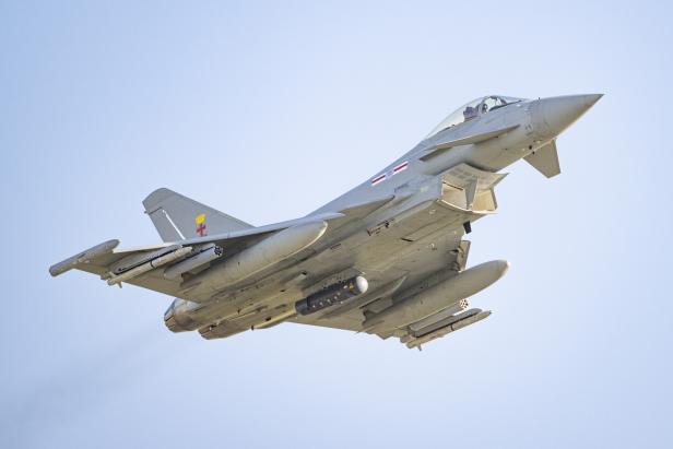 Eurofighter Typhoon mit Raketen und Zusatztanks im Flug vor blauem Himmel.
