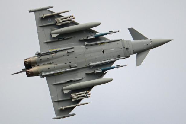 Ein Kampfjet mit Raketen und Bomben bewaffnet fliegt vor grauem Himmel
