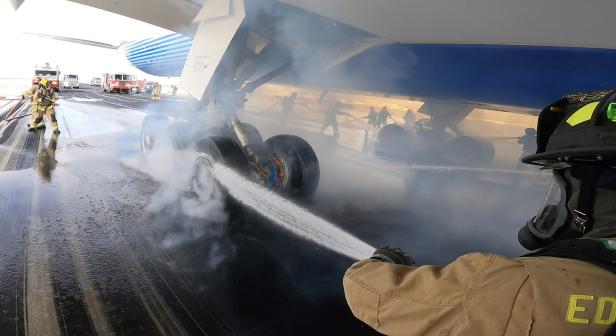 Feuerwehrleute löschen qualmende Flugzeugräder nach einem Bremstest auf dem Rollfeld.