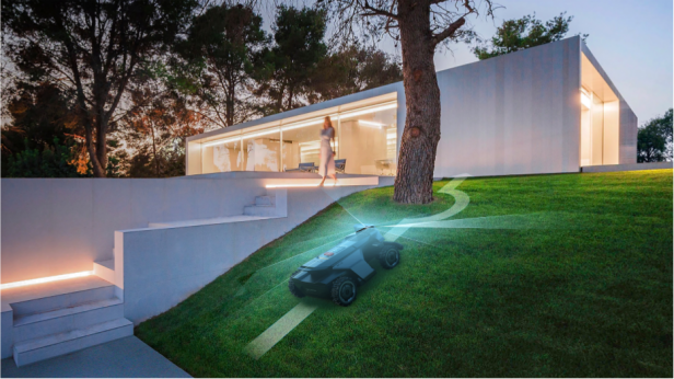 Ein moderner Navimow Mähroboter mit Allradantrieb mäht selbstständig eine steile Rasenfläche vor einem beleuchteten, modernen Haus und umfährt dabei geschickt einen Baum.