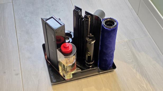 Zerlegter Dyson PencilWash mit Bürstenwalze und Wassertank auf einer Abtropfschale.