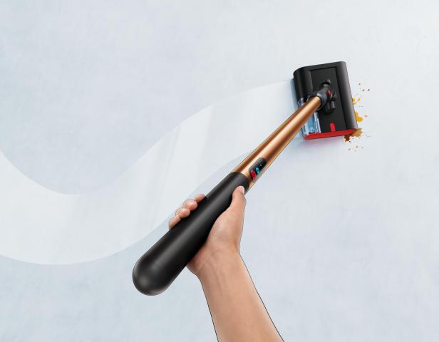Hand führt einen schlanken Nassreiniger über einen Boden mit sichtbarem Schmutzfleck.