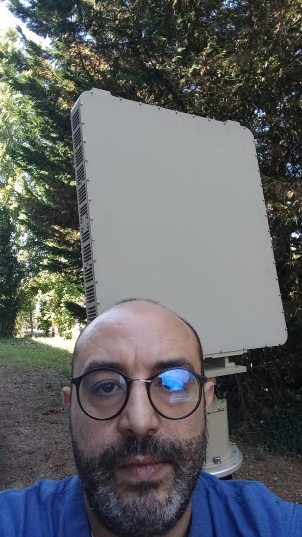 Mann mit Brille vor großem rechteckigen Radargerät im Freien.