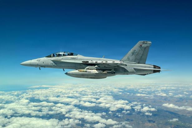 Kampfjet der US Navy fliegt über einer Wolkendecke bei klarem Himmel.