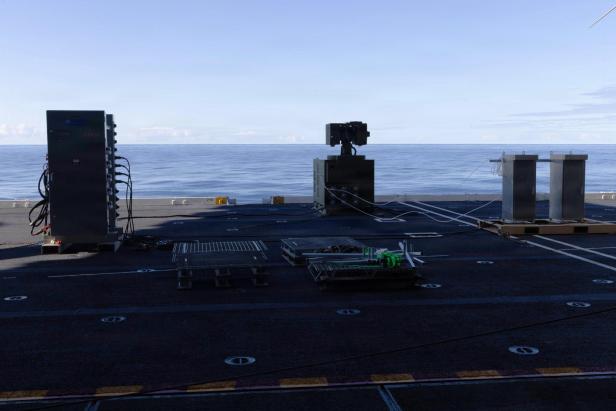Ein Container der Laserwaffe LOCUST steht im Schatten am Flugdeck eines Flugzeugträgers
