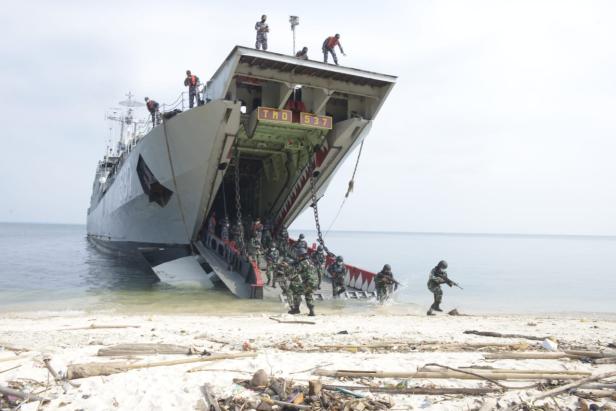 Soldaten verlassen ein Landungsschiff über eine geöffnete Bugrampe und stürmen an den Strand.