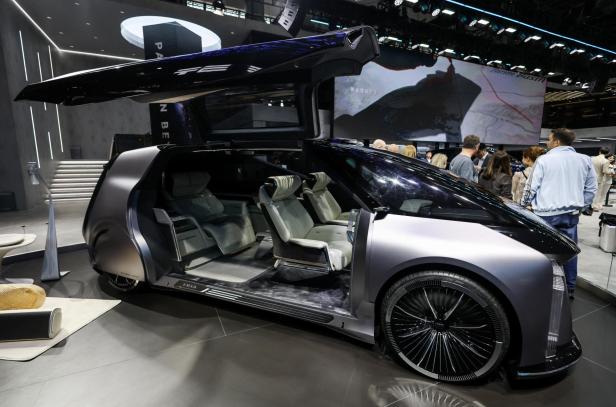 Ein futuristisches Auto mit Flügeltür und luxuriösem Innenraum steht offen auf einer Messe, umgeben von Besuchern.