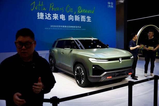 Ein futuristischer SUV mit kantigem Design steht auf einer Messe, zwei Männer unterhalten sich daneben.
