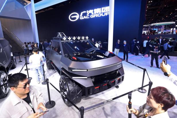Ein futuristischer, kantiger Geländewagen mit großen Reifen wird auf einer Automesse von vielen Menschen betrachtet und fotografiert.