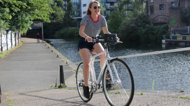 Frau fährt mit einem umgerüsteten E-Bike am Flussufer entlang.