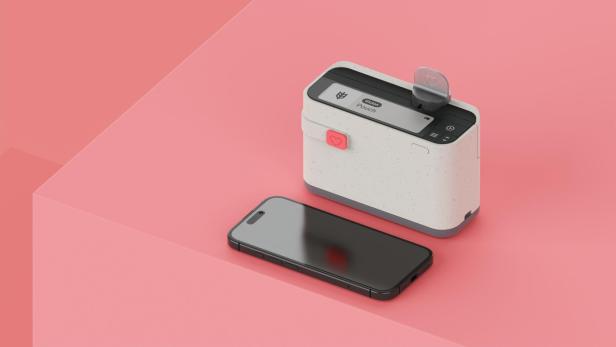 Ein schwarzes Smartphone liegt neben einem kompakten, weißen Gerät mit Display und Knöpfen auf rosa Untergrund.