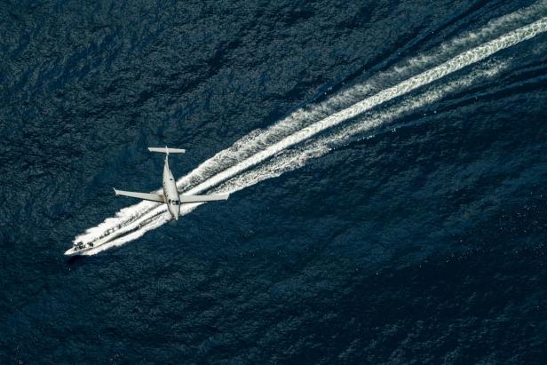 Ein U-28A Draco Flugzeug fliegt über ein Schnellboot auf offenem Meer.