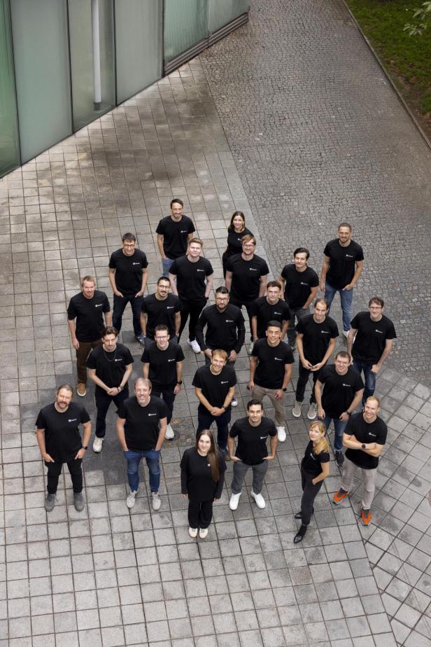 eine Gruppe Menschen in schwarzen Shirts steht in einem Hof und blickt nach oben