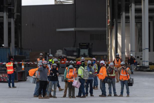 Eine Gruppe Bauarbeiter in Sicherheitskleidung steht auf einer Baustelle vor einem großen Gebäude.