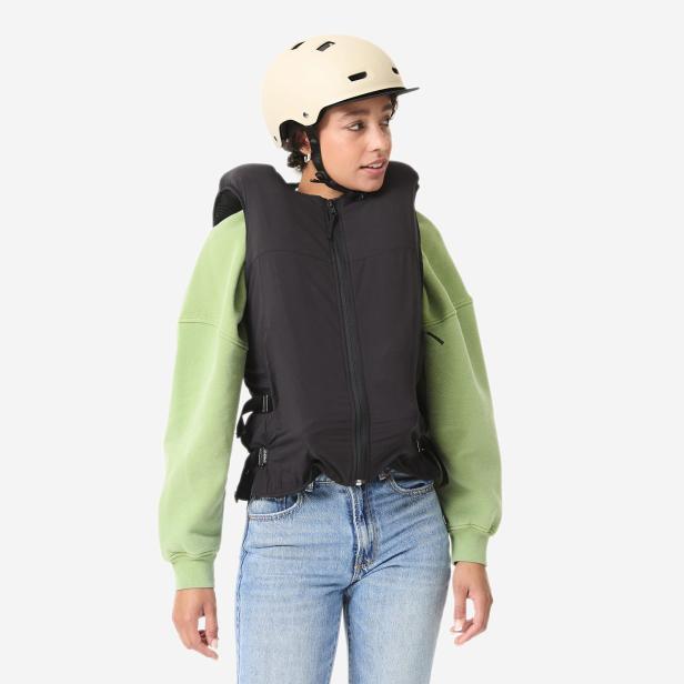 Eine Frau trägt die schwarze, ärmellose Airbag-Weste von Decathlon und In&motion mit sichtbarer Elektronik am Rücken.