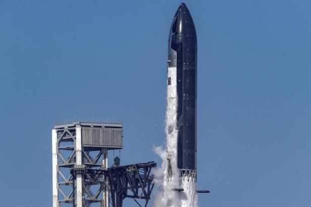 Die SpaceX Starship-Rakete hebt vor einem blauen Himmel von der Startrampe ab, während weißer Dampf aus dem Triebwerksbereich austritt.