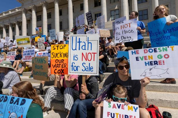 Viele Menschen sitzen auf Treppen und halten Protestschilder gegen den Verkauf von Wasser und Datenzentren in Utah hoch.