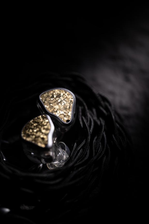 Die Moondrop Armature Art 24 In-Ear-Kopfhörer mit goldfarbenem Design und hochwertigem Kabel liegen auf dunklem Untergrund.