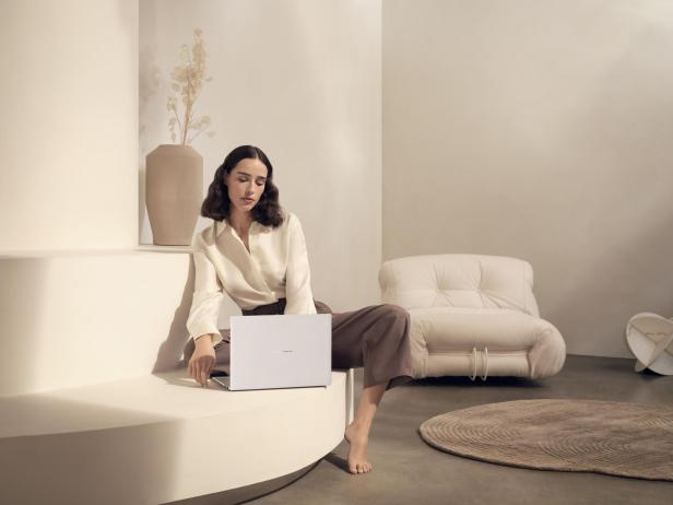 Frau sitzt in minimalistisch eingerichteter Umgebung und arbeitet an einem weißen Notebook.