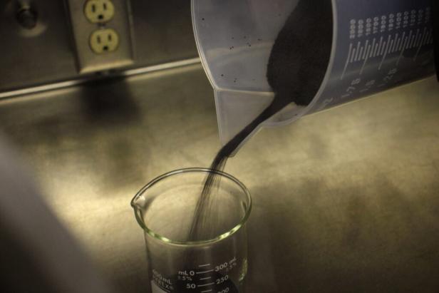 Schwarze Partikel, mit der Größe von Mohnsamen, werden aus einem Krug in ein Gefäß geleert